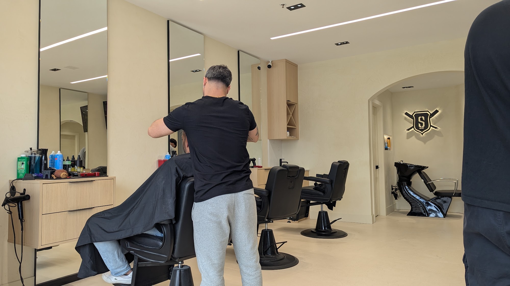 Barber working at Supreme Cuts Woodbridge, black chairs, cream walls, illuminated shield logo