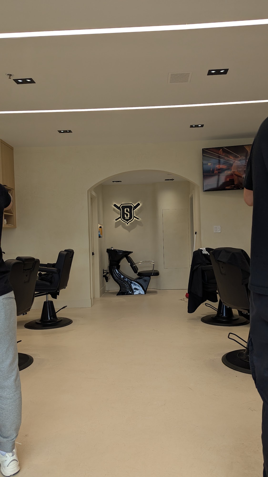 Supreme Cuts interior: archway with illuminated shield logo, black wash basin, cream walls
