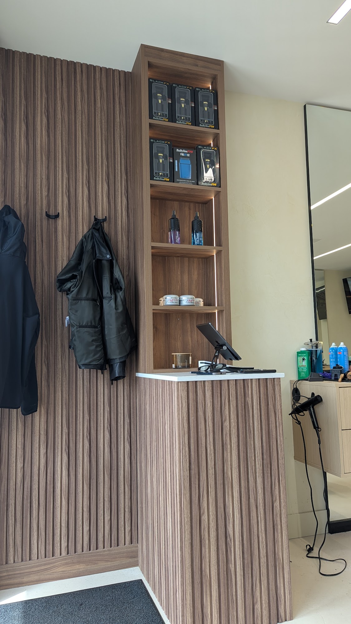 Reception area at Supreme Cuts: walnut fluted panels, retail shelf, BaByliss Pro clippers